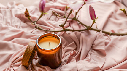 Aromatherapy candle with magnolia branches on soft pink fabric, creating a serene atmosphere © shine.graphics