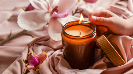 Lighting a scented candle with a match on a soft pink fabric with magnolia flowers © shine.graphics