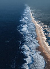 Fototapeta premium Aerial View of Ocean Waves Crashing on a Sandy Beach Shoreline.