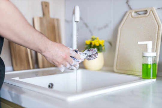 Person lathering utensils under running faucet in kitchen sink