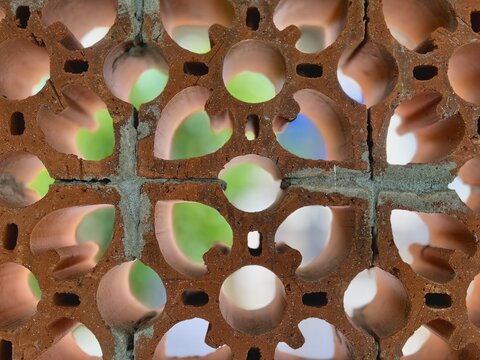 Detailed view of perforated red bricks with circular openings, showcasing architectural design, airflow structure, and natural earthy tones.