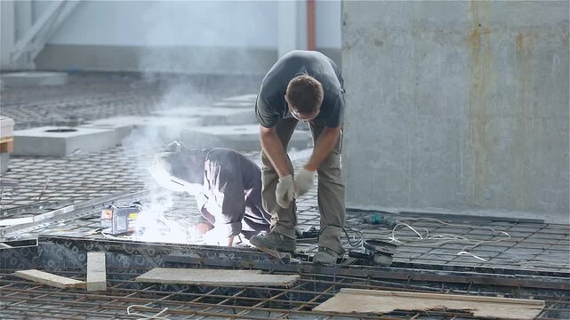 Installation of reinforced concrete floors in a large industrial or commercial building. Workers welds metal reinforcement and prepares the building's floors for concrete pouring.