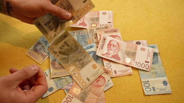 Hands drop Serbian dinar banknotes onto a sofa, showing 1000 and 2000 dinar bills. Cash flow and personal finance concept for budgeting, spending, saving, banking and inflation