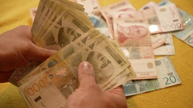 Hands count Serbian 2000 dinar banknotes over mixed cash on a sofa. Budget planning and cash handling concept for savings, salary, spending, banking and personal finance