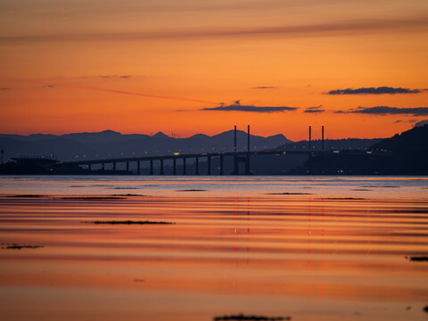 Sunset silhouette of Kessock Bridge and mountains over Beauly Firth, Inverness, Scotland.