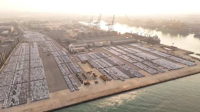 new cars and heavy agricultural machinery parked in lines at an automotive port terminal or factory lot. Vehicle export, import logistics, and automotive manufacturing industry.