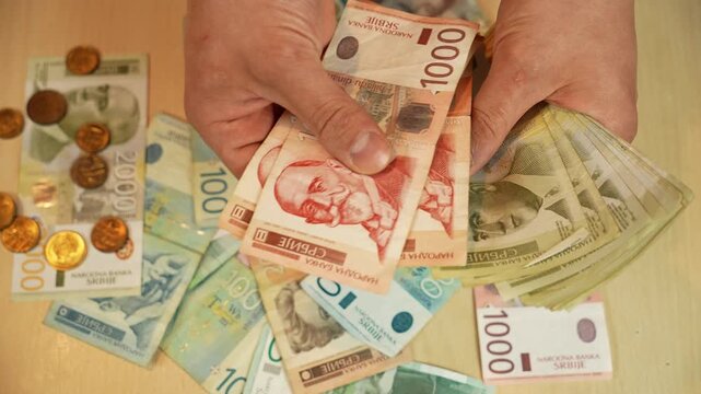 Hands count Serbian 1000 and 2000 dinar notes above mixed cash and coins. Money handling and budget control concept for savings, spending, banking and personal finance