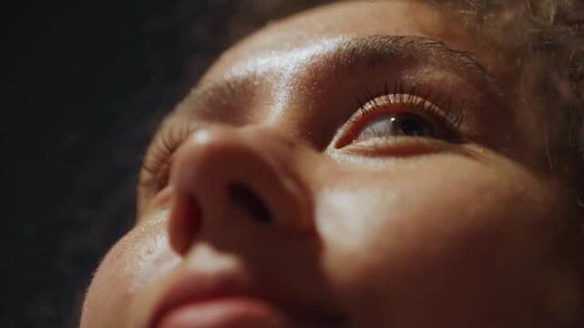 Closeup face gazing upward soft light, dewy skin catching highlights, eyelashes and nose in sharp focus, curly hair halo at edge, lowkey cinematic mood, subject shifting between poet stargazer dreamer