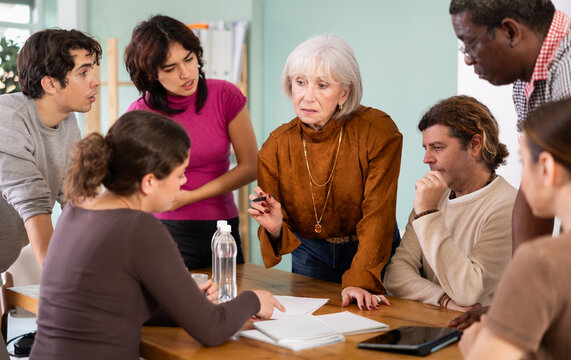 Focused men and women of different ages actively communicating and sharing ideas at table