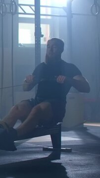 Focused athlete training on indoor rowing machine in dimly lit gym, showcasing intense full body workout, endurance exercise and powerful fitness determination