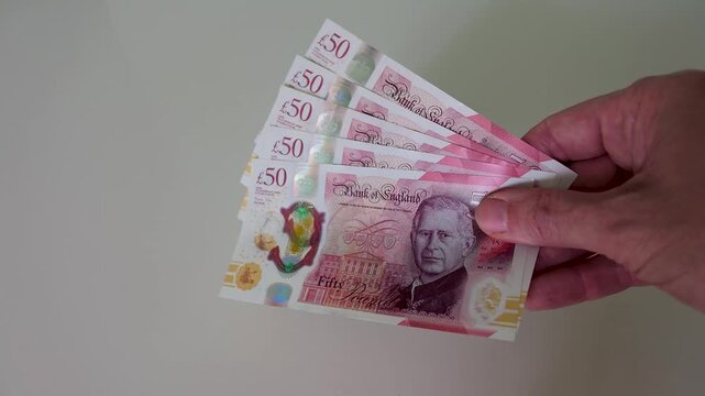A hand enters frame and brings five fanned out British polymer &pound;50 notes totalling &pound;250 to the centre, holding them steady in slow motion against a clean white background.