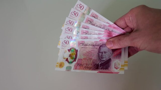 A hand enters frame and brings six British polymer &pound;50 notes totalling &pound;300 to the centre, holding them steady in slow motion against a clean white background.
