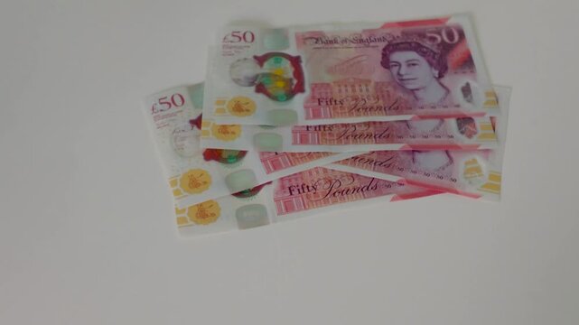 A hand drops a &pound;50 note onto a white surface then methodically counts out a full &pound;500 in polymer &pound;50 notes, building a loosely stacked, dishevelled pile in slow motion.