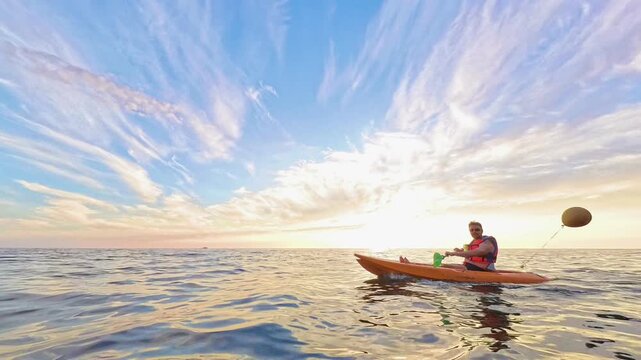 Kayak sunset ocean man paddles his orange boat across the calm sea during a beautiful evening for recreation and adventure
