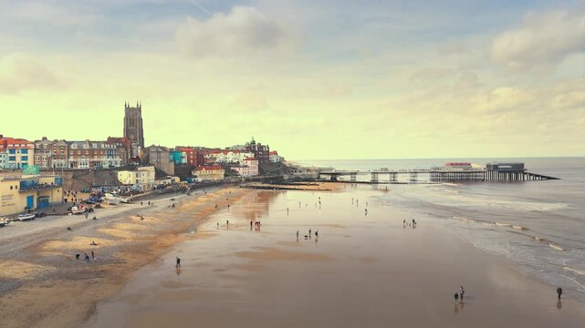 Seaside views of the holiday town of Croma on the Norfolk coast. Sandy beach and sea. Holiday destination, vintage photograph. North Sea coastline, Chapel, church and pier on the promenade, tourists.