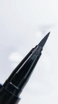 Opening a black eyeliner cap in extreme close up on white background, showing eye cosmetic detail clearly, suitable for women beauty themes and makeup advertising.