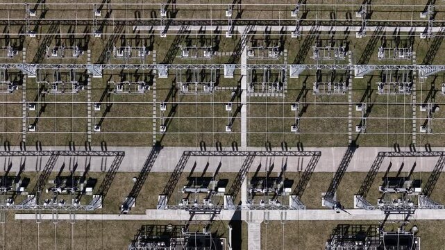 An overhead drone view captures the complex geometric patterns of an industrial electrical substation during a bright sunny day.