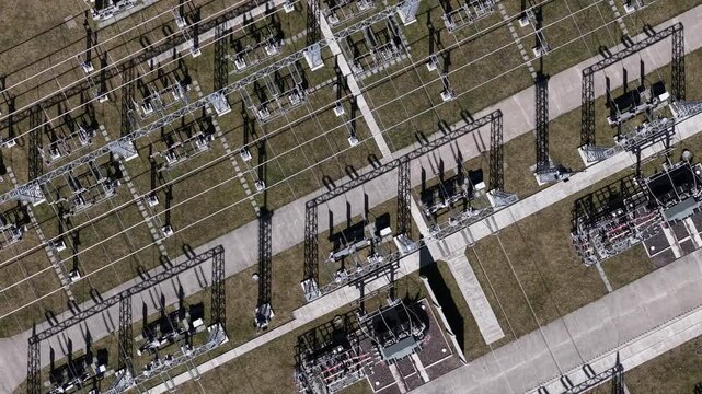 An aerial view shows an electrical substation facility with complex metal structures and transformers distributing power across a regional grid.