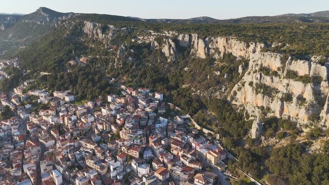 Cinematic wide shot of the historic mountain town Baunei during golden hour, showcasing authentic Mediterranean architecture and dramatic rocky terrain.