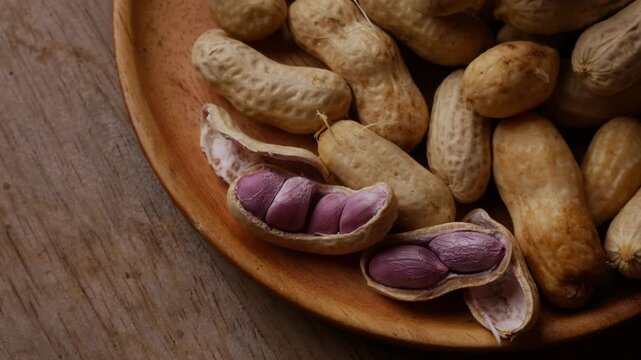 Boiled peanuts in shell with purple violet skin kernels revealed on wooden plate on rustic wood table, healthy traditional Asian snack nutrition closeup