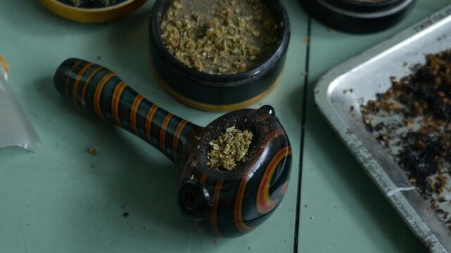 Glass Hand Pipe with Colorful Striped Design and Herb Grinder on Teal Table for Cannabis Lifestyle