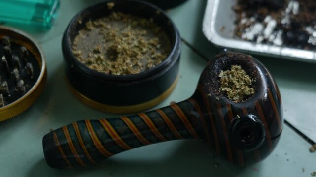 Glass Hand Pipe with Colorful Striped Design and Herb Grinder on Teal Table for Cannabis Lifestyle