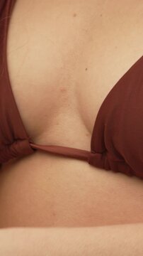 Woman bikini close-up featuring a female body in a brown ribbed swimsuit as she adjusts her chest for body positivity