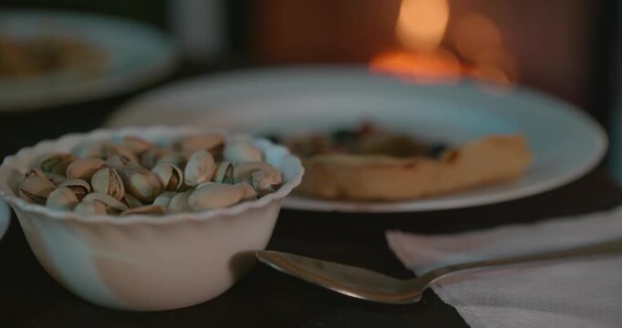 Close-up Bowl with Pistachios on Table Near Fireplace. 4K 10-bit