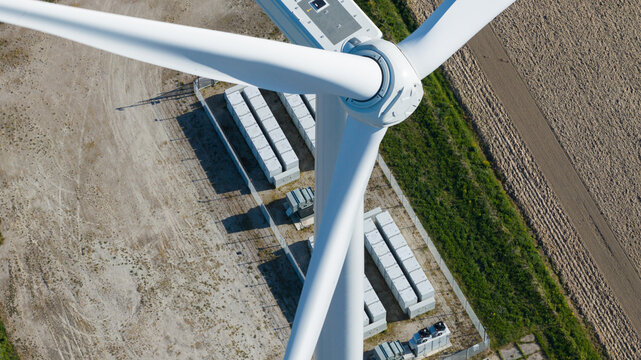 Aerial view of a wind turbine nacelle and blades overlooking a battery energy storage system on the ground in Ooltgensplaat, Zuid-Holland, Netherlands.