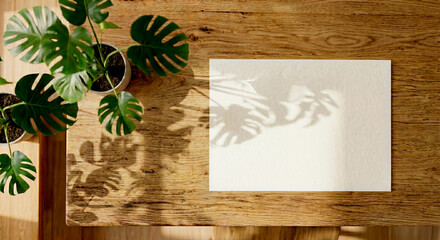 Mockup de papelería en blanco sobre mesa de madera rústica con luz natural y sombras de plantas, interior cálido. © Manuelexequiel