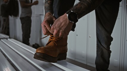 Fototapeta premium Close Up of Industrial Safety Boots. Worker In Professional Locker Room Ties Laces of Heavy Duty Brown Leather Safety Boots, Focusing on Footwear Reliability, Workplace Safety. Industrial Preparation.