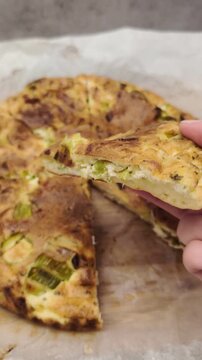 Woman's hand taking a piece of a freshly baked frittata with leeks and cheese. Nutritious homemade meal, ideal for a healthy diet