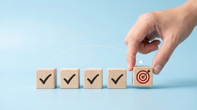 Hand positions a wooden block featuring a target icon onto a line of finished tasks marked with checkmarks to represent the successful completion of a goal-oriented project plan in a business setting.