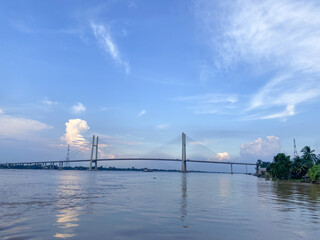 Fototapeta premium Magnificent view of a bridge spanning a wide river at sunset, with lush green landscapes and a vibrant sky, capturing urban connectivity and natural beauty.