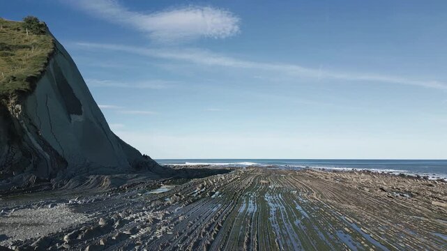 Incredible geological flysch rock formations extending from a cliff into the Cantabrian sea on the famous Sakoneta beach, part of the Basque Coast UNESCO Global Geopark in Zumaia, Spain