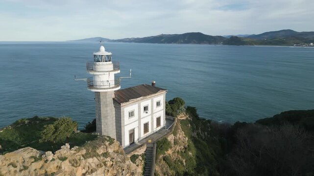 Majestic aerial view of the historic lighthouse of Getaria, located on a cliff overlooking the calm Cantabrian Sea in the Basque Country, with the beautiful coastline visible in the distance