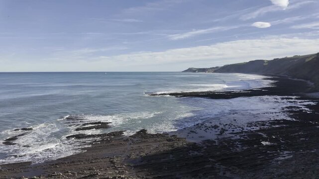 Beautiful coastal landscape showing the flysch rock formations at Sakoneta beach in the Basque Coast Geopark, with ocean waves crashing against the rocky shore under a blue sky