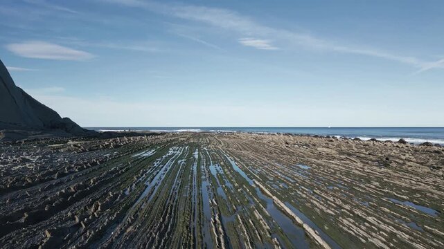 Stunning aerial view of the unique flysch rock formations at Sakoneta beach in the Basque Country, Spain, with layers of sedimentary rock stretching towards the Atlantic Ocean on a sunny day
