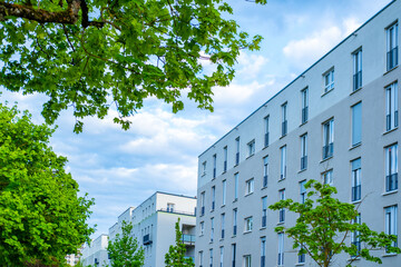 Modern apartment buildings, light beige facades, blue sky with clouds, green trees, urban residential area, european clean architecture, well-maintained landscape, apartment buildings city lifestyle © kittyfly