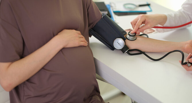 Doctor teaching patient use of digital blood pressure monitor, clinician guiding on cuff placement, reading interpretation. Blood pressure during pregnancy