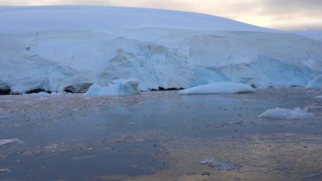 A first-person point-of-view (POV) from a Zodiac boat navigating through brash ice and icebergs toward the towering blue ice face of a tidewater glacier in Foyn Harbour, Antarctica