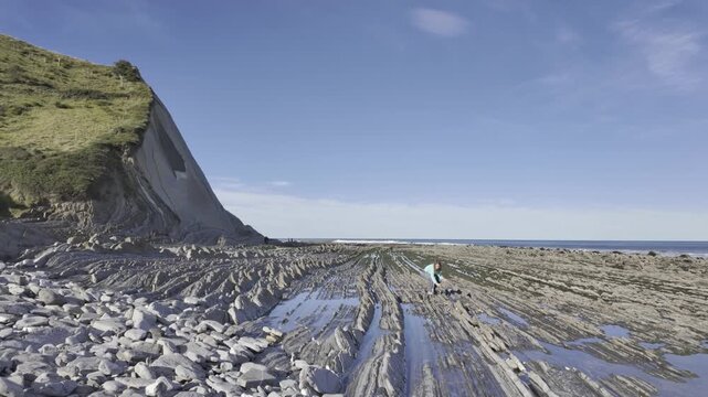 Young woman exploring the incredible flysch formations on the beautiful Sakoneta Beach, located on the Basque Coast Geopark in Zumaia, during a sunny day with clear blue sky