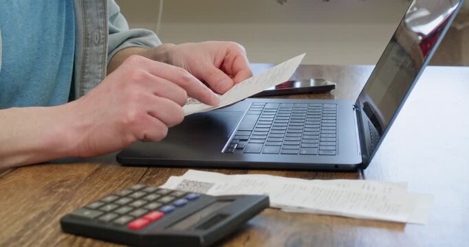 Businessman hands hold bill and calculate total amount at workplace closeup. Man tenant with laptop checks living expenses growth working from home office