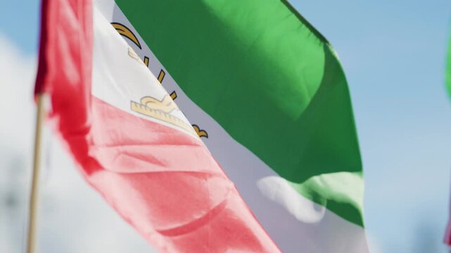 Colorful Iranian flag with lion emblem waving against clear blue sky