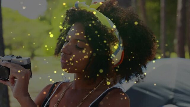 Woman raising camera to eye, adjusting and shooting photos at campsite with golden sparkle overlay
