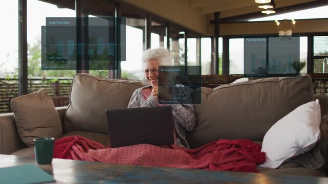 Senior woman sitting sofa with phone watching laptop, call causing HUDs rising for data monitoring
