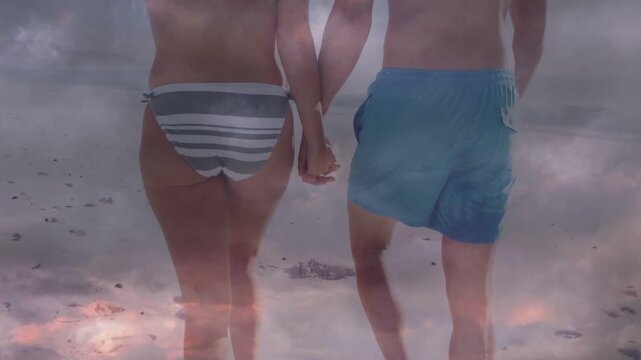 Man and woman handholding initiating walking on beach, cloud overlaying pair for travel