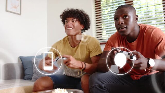 Two male players pressing controllers in living room, gaming as HUD icons floating across, smiling