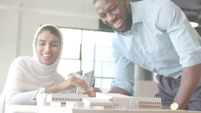 Woman in scarf and man leaning shaking hands adjusting scale model with animated callout for design