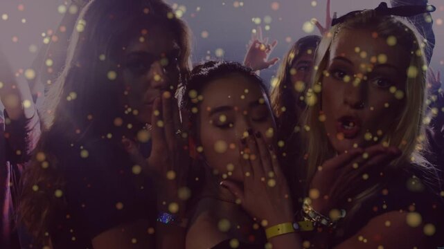3 women posing, mingling in club as crowd raises hands revealing man, gold bokeh overlaying faces